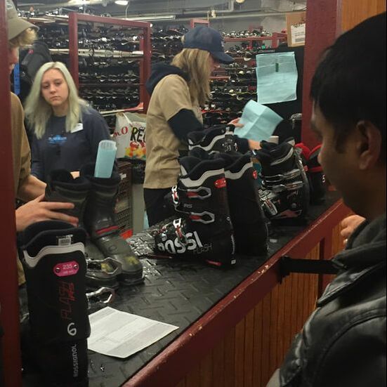 Picture of guests standing at the counter in the rental area. Employees gather boots and equipment for guests to rent, ensuring that it is adjusted and the correct size for Pine Knob guests.