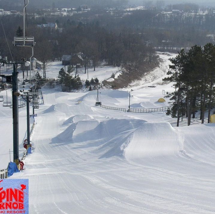 Picture of the terrain park at Pine Knob, It is a snowy hill filled with features like mini-hills and pipes that skiers and snowboarders can do tricks on. There are trees and a chairlift around this area as well.