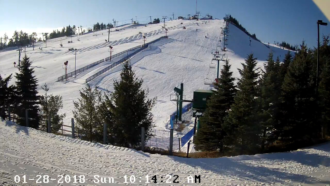 Picture of the Pine Knob ski hill covered in snow. The sky is blue and there are pine trees. 