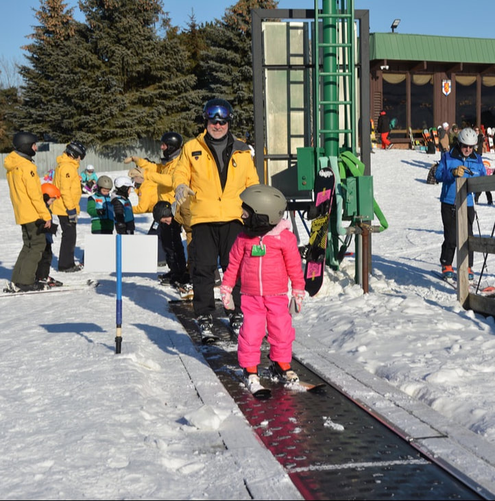 Picture of a Pine Knob Ski Instructor helping a young student on to the beginner lift during a ski lesson.
