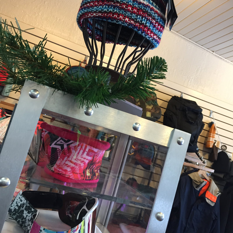 Picture of a product display in the ski and snowboard shop at Pine Knob. Inthe case there are scarves and goggles, Hats and coats are also on display. Items are colorful.